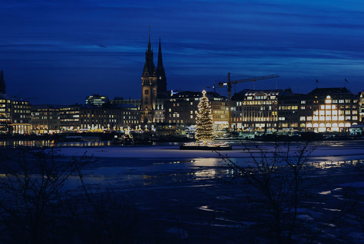 Die beleuchtete Alstertanne auf der Binnenalster zur blauen Stunde, dahinter die erleuchtete Hamburger Innenstadt.
